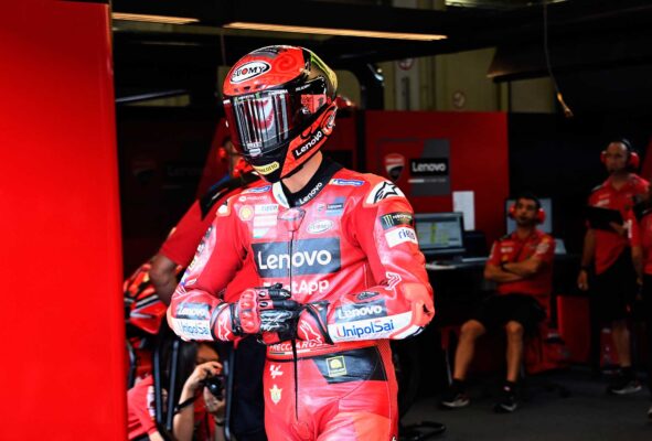 Ein Fahrer des Ducati Lenovo Teams in der Box, in einem mit Sponsorenlogos bedeckten Anzug